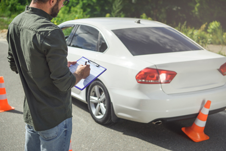 man writing on clipboard while standing near a car on road