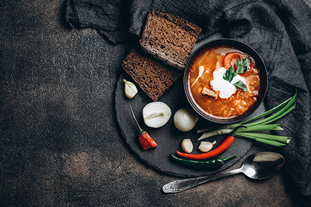 Traditional Ukrainian Russian red soup borscht with ingredients, spice and herbs in the bowl on a da