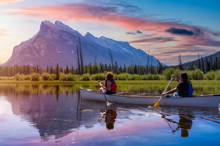 Couple adventurous friends are canoeing in a lake surrounded by the Canadian Mountains. Colorful Sun