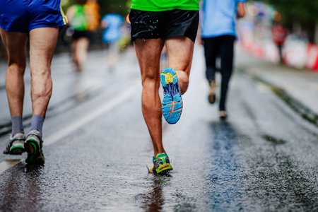 Marathon running race, people feet on city road in wet rain