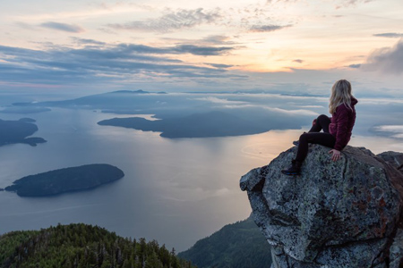 Adventurous Female Hiker on top of a mountain covered in clouds during a vibrant summer sunset. Take