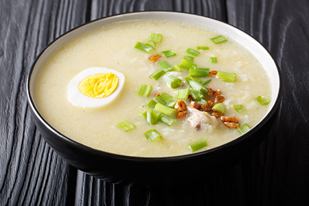 Hot Arroz Caldo traditional rice soup with chicken, vegetables and egg close-up in a bowl on the tab