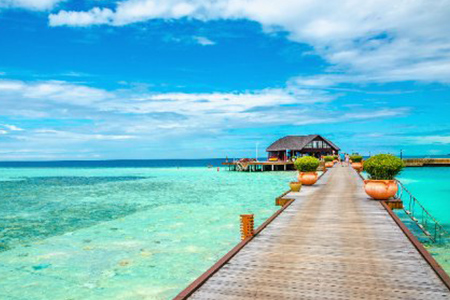 Wooden bridge leading to an exotic bungalow on the background of azure water, maldives