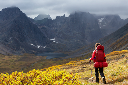 Woman backpacking on scenic hiking trail to lake surrounded by mountains during fall in canadian nat