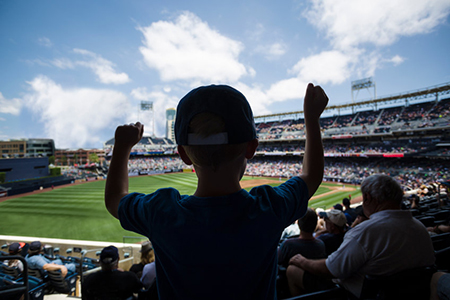 Child standing and cheering at a baseball game. Silhouette view from behind