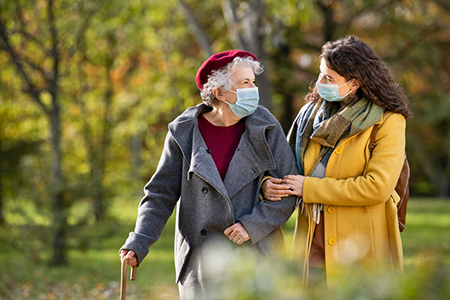 Elderly grandmother in protective mask holding stick enjoying with granddaughter in park.