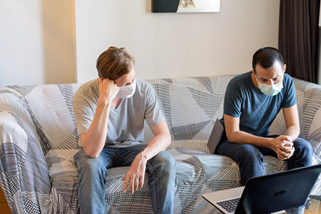 Two stressed multi ethnic men with mask as friends looking depressed while video calling at home und