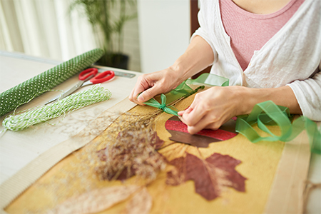 Close-up shot of a woman sitting at wooden table and decorating bouquet of withered flowers with gre