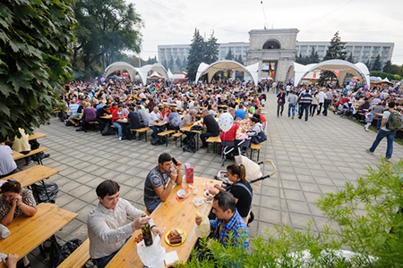 large group of people sitting at outdoor festival with food and wine