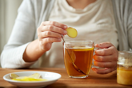 close up of woman adding ginger to tea cup with lemon and honey