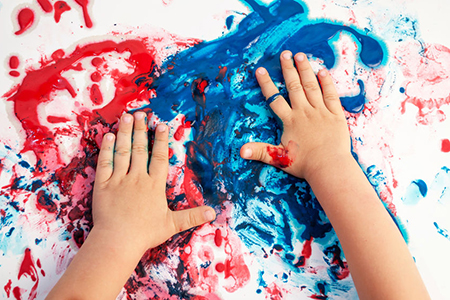 Painted hands smudging colors on messy paper .