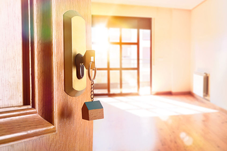 Open entrance door detail of a house with keys in the lock and empty room in the background with gol