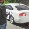 man writing on clipboard while standing near a car on road