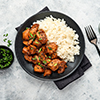 Spicy teriyaki chicken fillet pieces with rice, green onions and black sesame seeds on black plate o