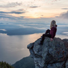 Adventurous Female Hiker on top of a mountain covered in clouds during a vibrant summer sunset. Take