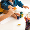 cropped view of brother and sister sitting at table and drawing with paints together