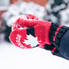 Close-up of hands in red Canada mittens make a snowball from snow on a blurred background with snow