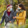 Elderly grandmother in protective mask holding stick enjoying with granddaughter in park.