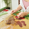 Close-up shot of a woman sitting at wooden table and decorating bouquet of withered flowers with gre