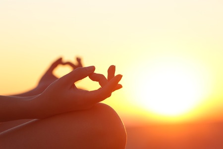 cropped image of hands in yoga pose with sunset in background