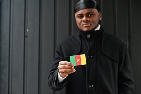 African man wear black durag hold Cameroon flag at hand isolated dark background.