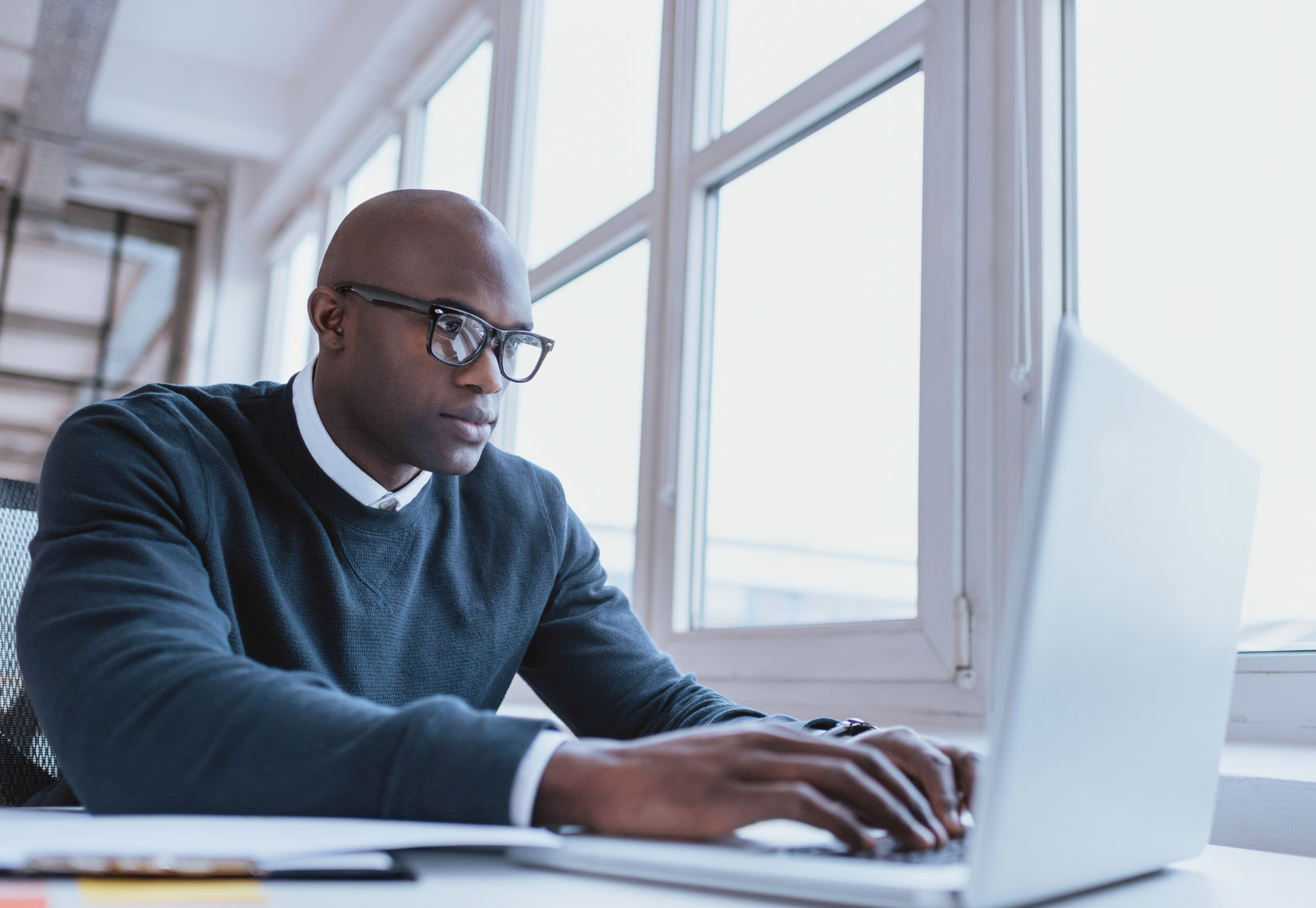 African american man in black glasses sitting at a desk working on a white laptop