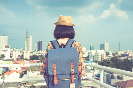 Back view of Asian woman traveler with backpack standing on the balcony with cityscape background