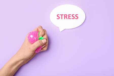 Female hand squeezing stress ball and word STRESS on color background