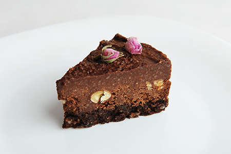 Slice of vegan chocolate nut cake on white blackground close-up