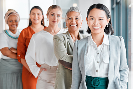 Portrait of smiling businesswomen standing in office with colleagues in background