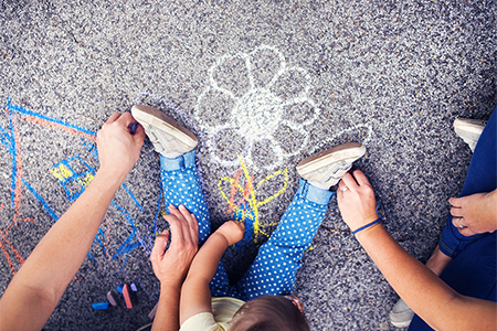 Close up of little girl and her parents drawing with chalks on the sidewalk