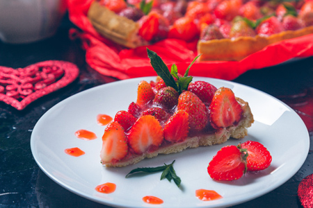 Strawberry tart with cream and mint on a black background.