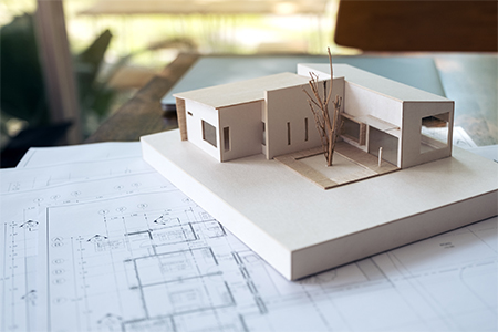 An architecture model with shop drawing paper and laptop on table in office with blur nature backgro