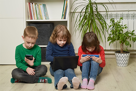 Children sit on the floor and use electronics