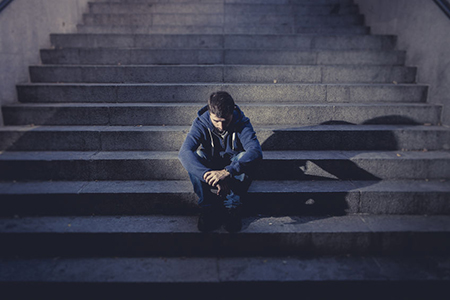 Young desperate man in casual clothes abandoned lost in depression sitting on ground street concrete