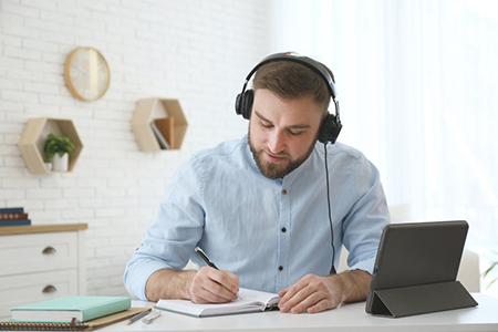 Young man taking notes during online webinar at table indoors