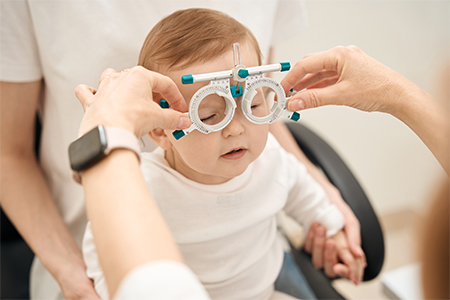 Eye doctor hands putting on ophthalmic trial frame on calm little child