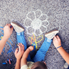 Close up of little girl and her parents drawing with chalks on the sidewalk