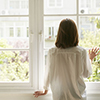 rear view of a young asian woman looking out of window at home