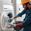 Repairman in worker suit with professional equipment is fixing washing machine in laundry room