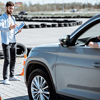 Male instructor teaching young woman driver to park a car on the training ground