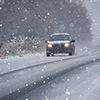 The car is driving on a winter road in a blizzard