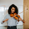 Young woman playing violin with writing board on the background in music studio