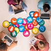 Top view of four young friendly people in casualwear sitting by multi-color papers with icons on the