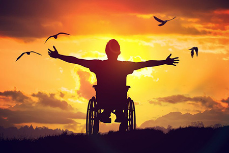 man in wheelchair stretching hands at sunset