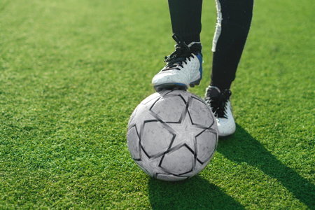 soccer player legs with ball on green grass background, football game