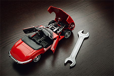 Concept of repair, A vibrant red sports car model rests on a polished wooden surface, its hood elega