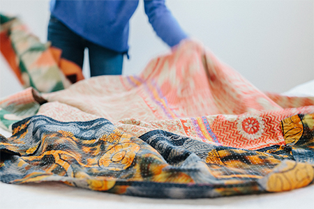 A person spreading a quilt fabric over a bed in a bedroom