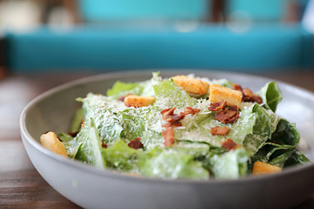 Caesar salad with crispy bread and bacon close up on wood background