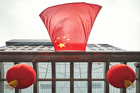Looking up at Chinese flag and red lanterns on a building.